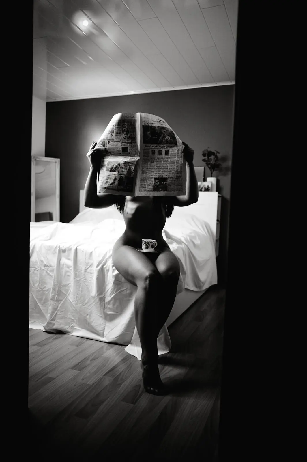 Emily sitzt mit einer aufgeschlagenen Zeitung auf dem Bett – Boudoir in Schwarz-Weiß