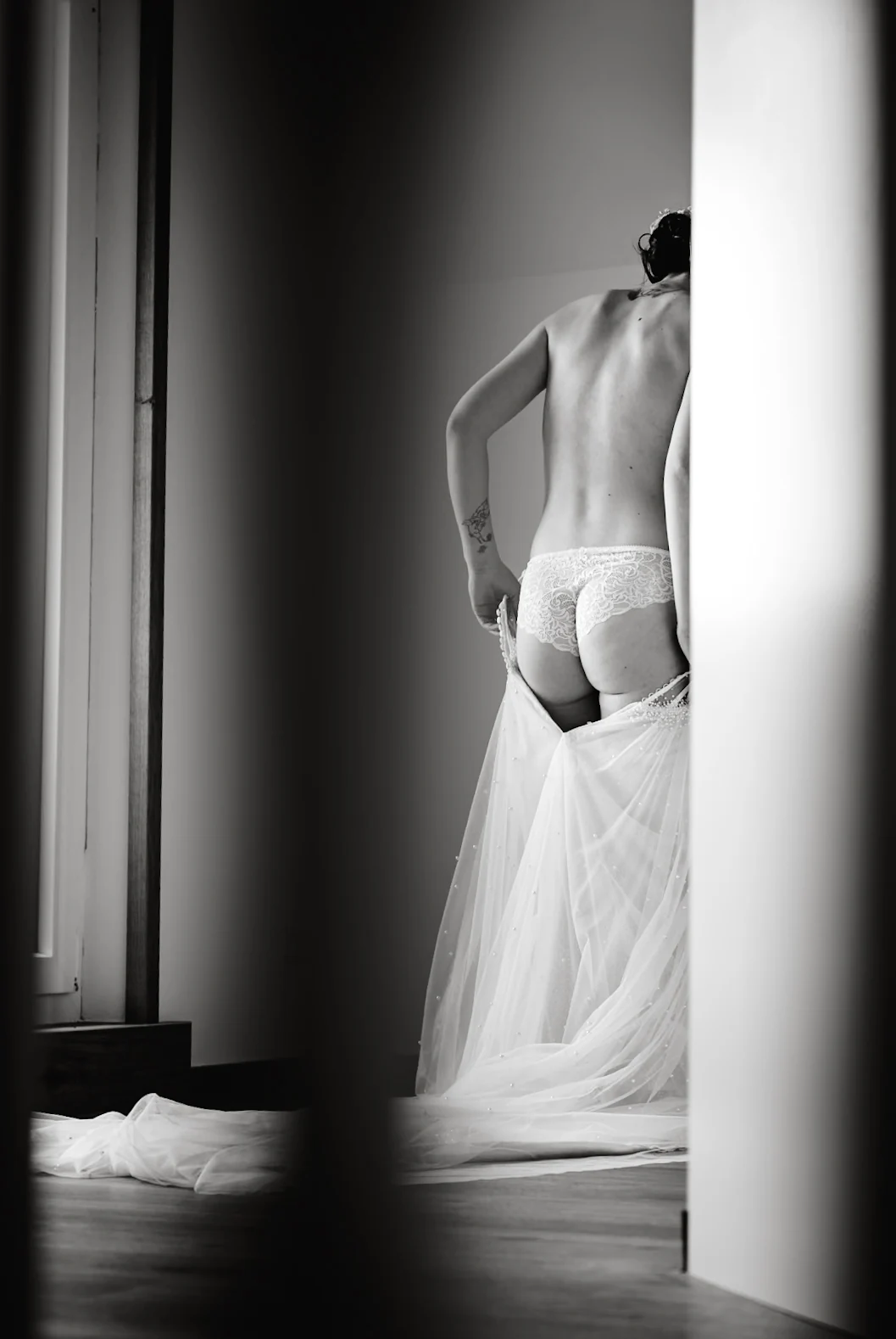 Braut beim Anziehen ihres Kleids am Fenster