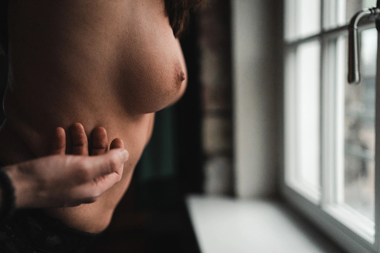 Eine Hand streicht im Fensterlicht über die nackte Brust