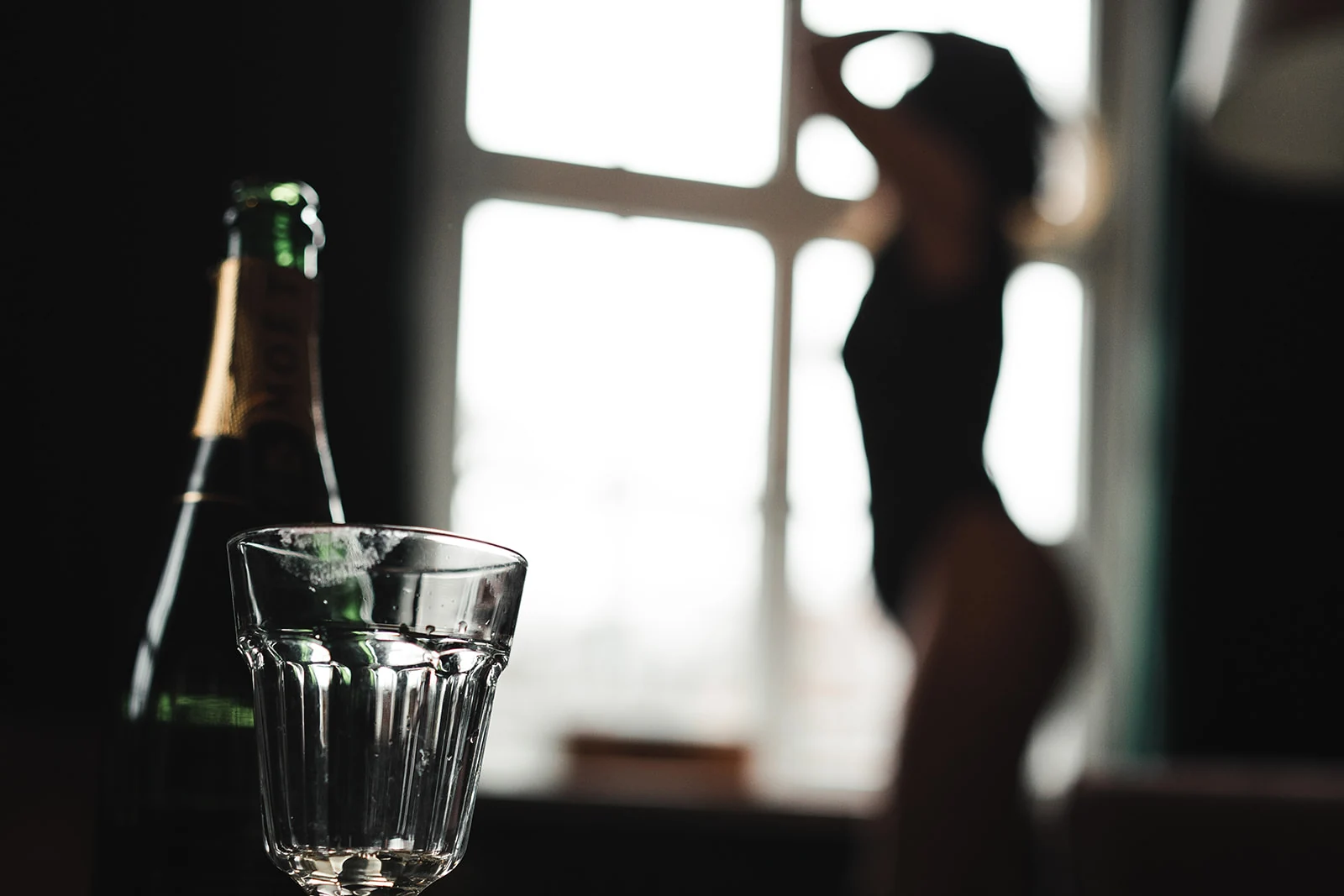 Sektflasche und Gläser im Vordergrund, ein Paar im Fensterlicht