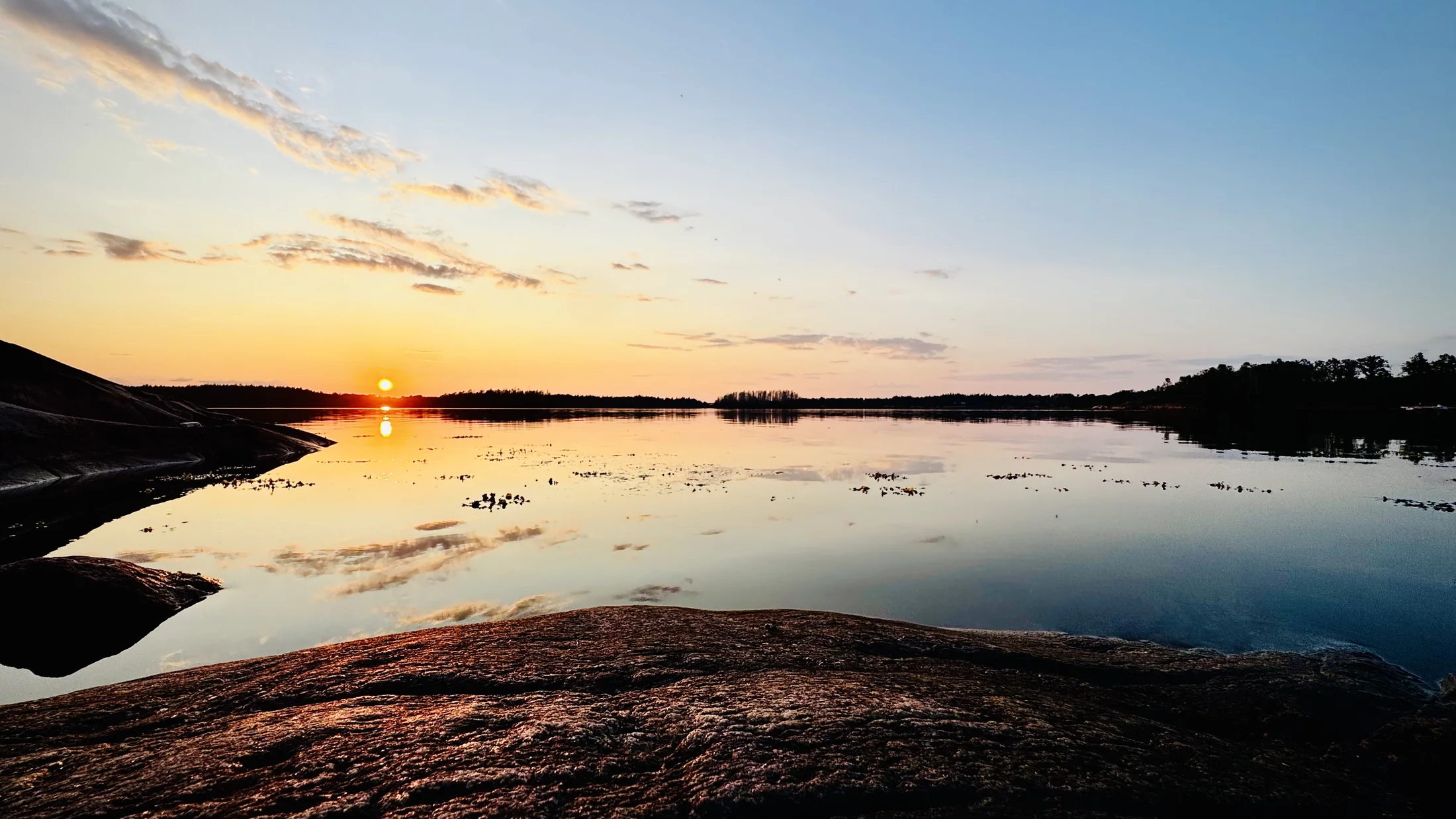 Ruhiger Sonnenuntergang über dem Wasser und den Felsen in Schweden