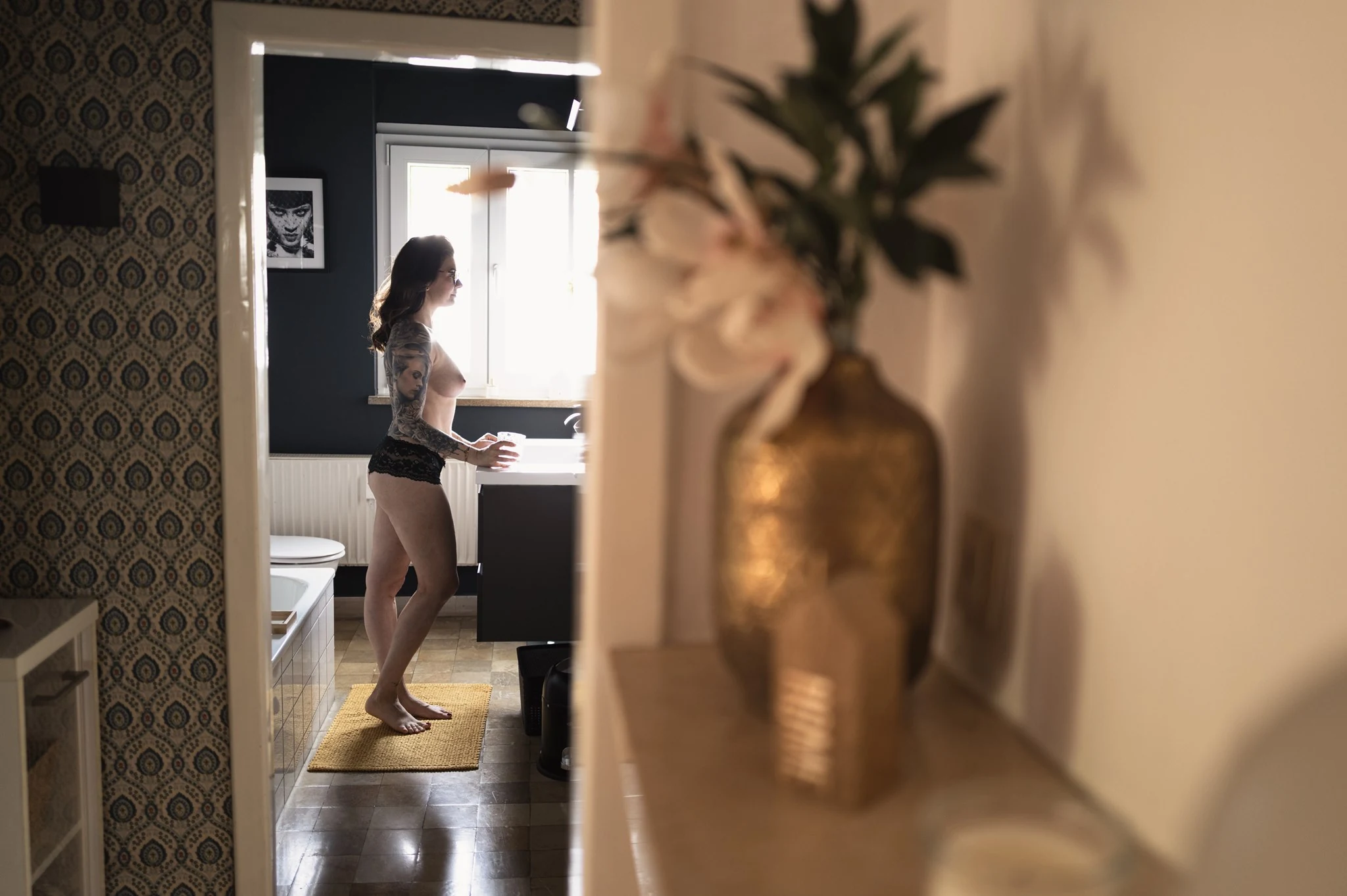 Blick durch die Tür auf Julia mit einem Glas am Waschbecken, Vase im Vordergrund