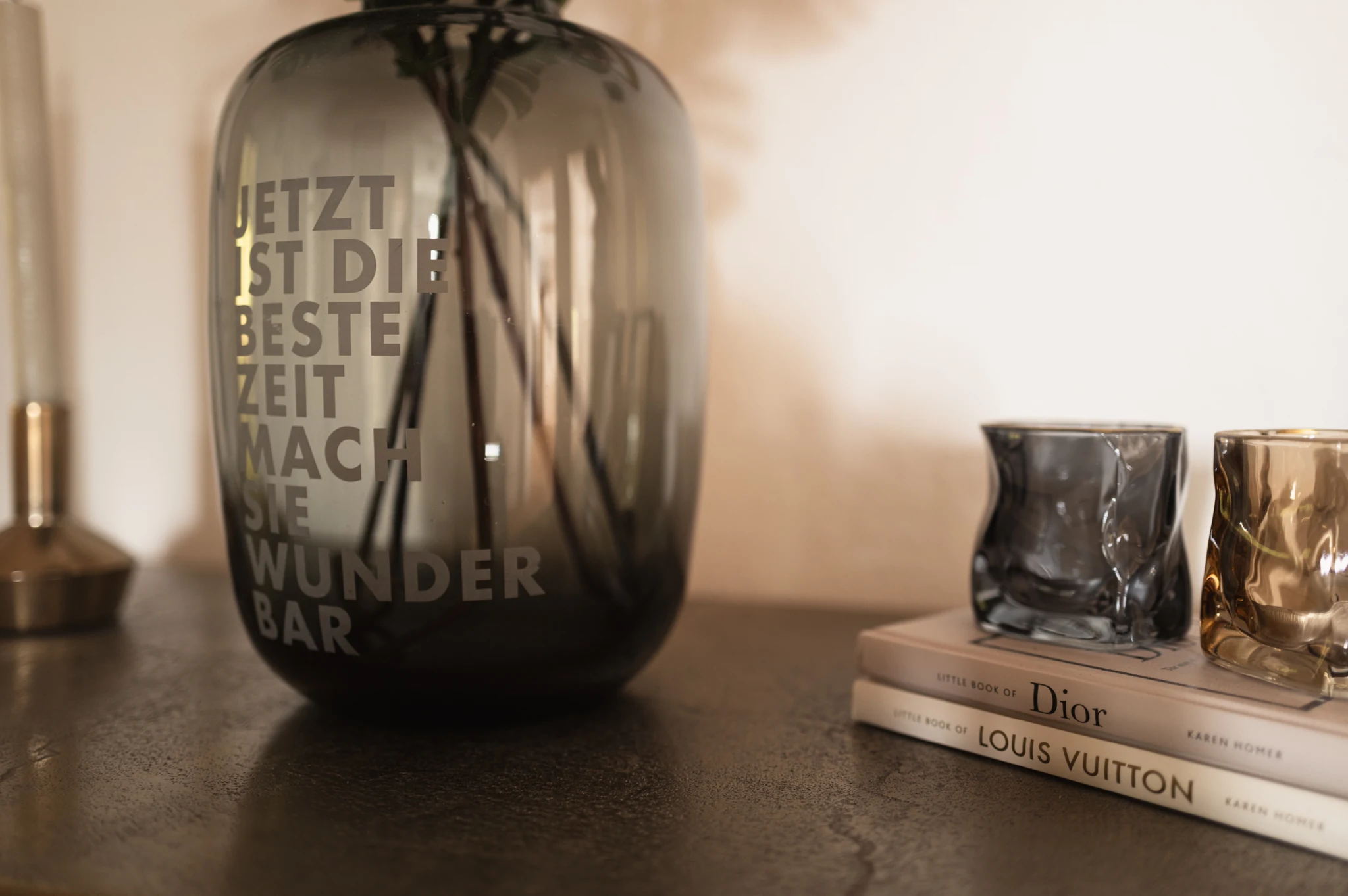 Vase mit dem Spruch Jetzt ist die beste Zeit, mach sie wunderbar; daneben Gläser und Modebücher