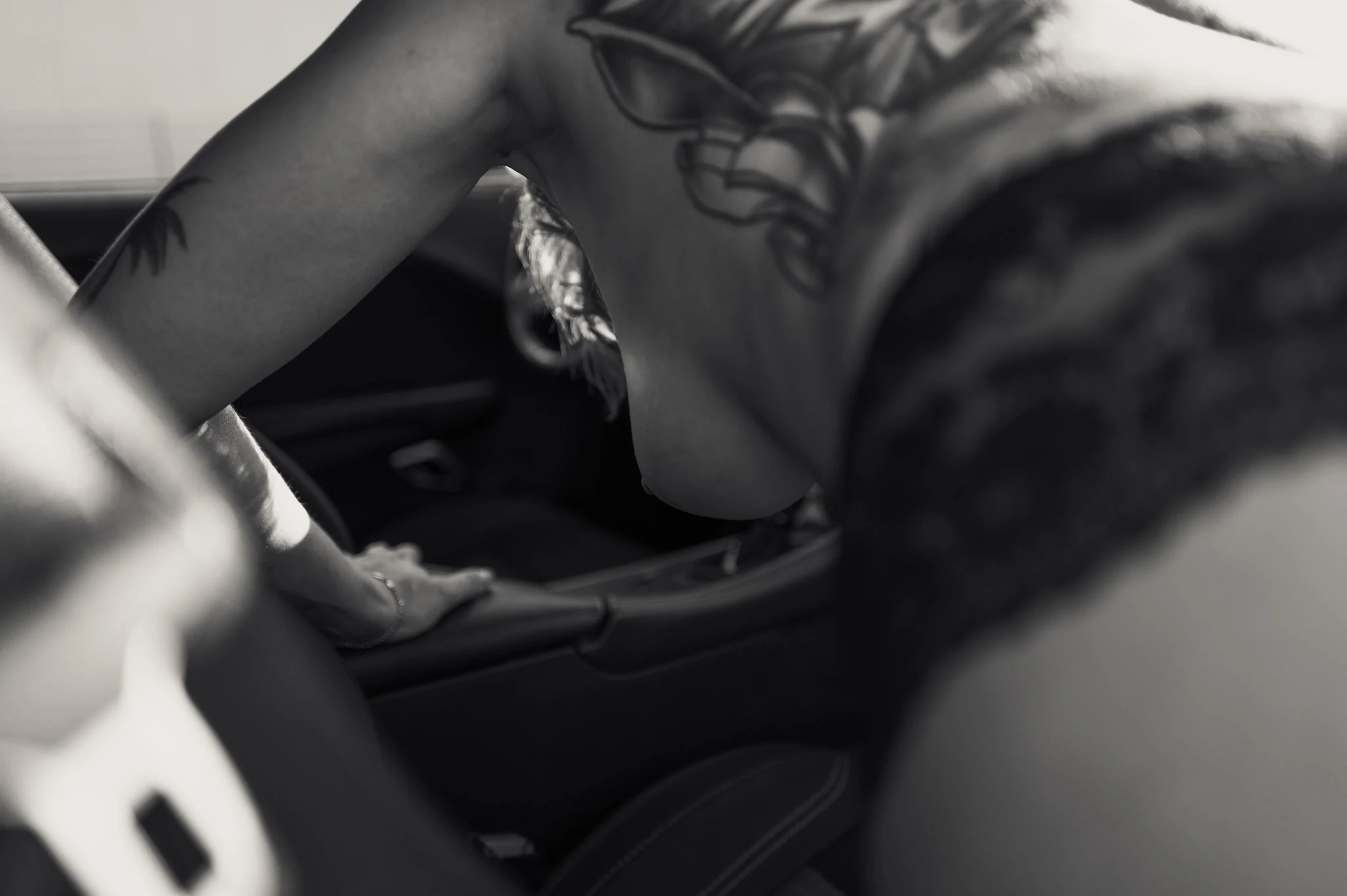 Julias tätowierter Oberkörper und Hand im Auto, Schwarzweiß