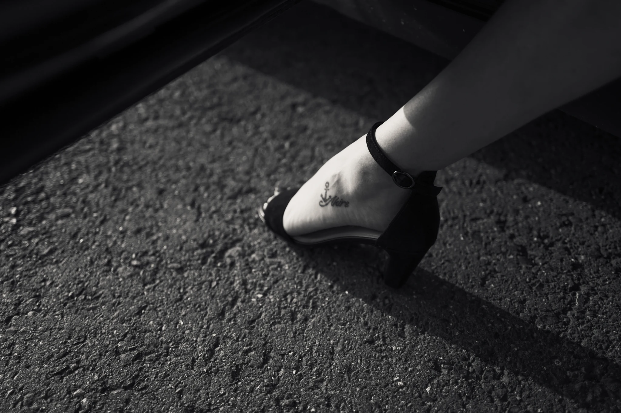 Julias Fuß mit Tattoo und schwarzem Absatzschuh auf Asphalt