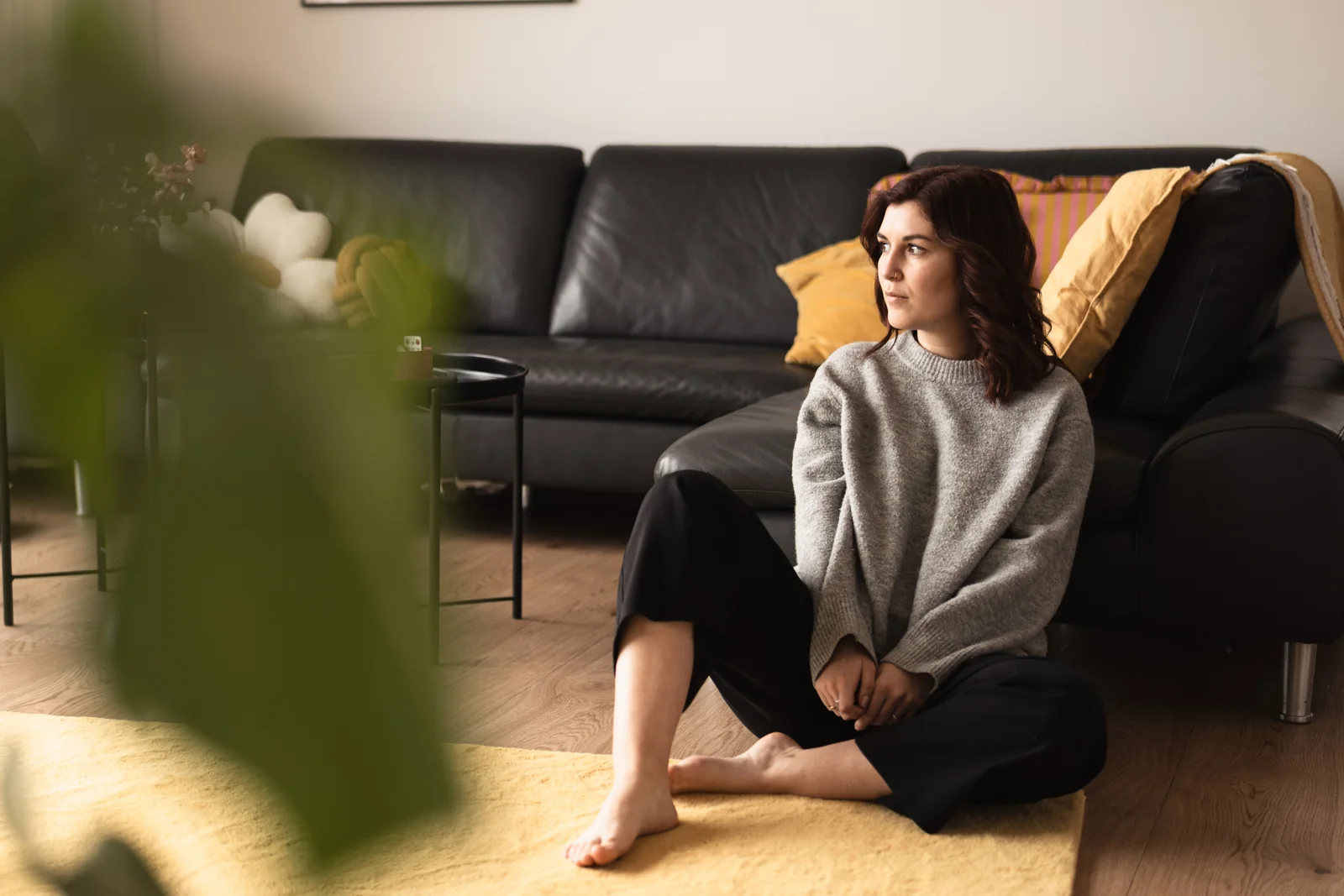 Eine Frau sitzt im großen Pullover auf dem Boden neben dem Sofa.
