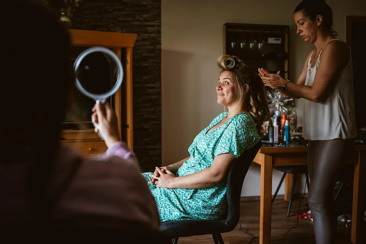 Die Braut sitzt beim Frisieren vor einem kleinen Spiegel.