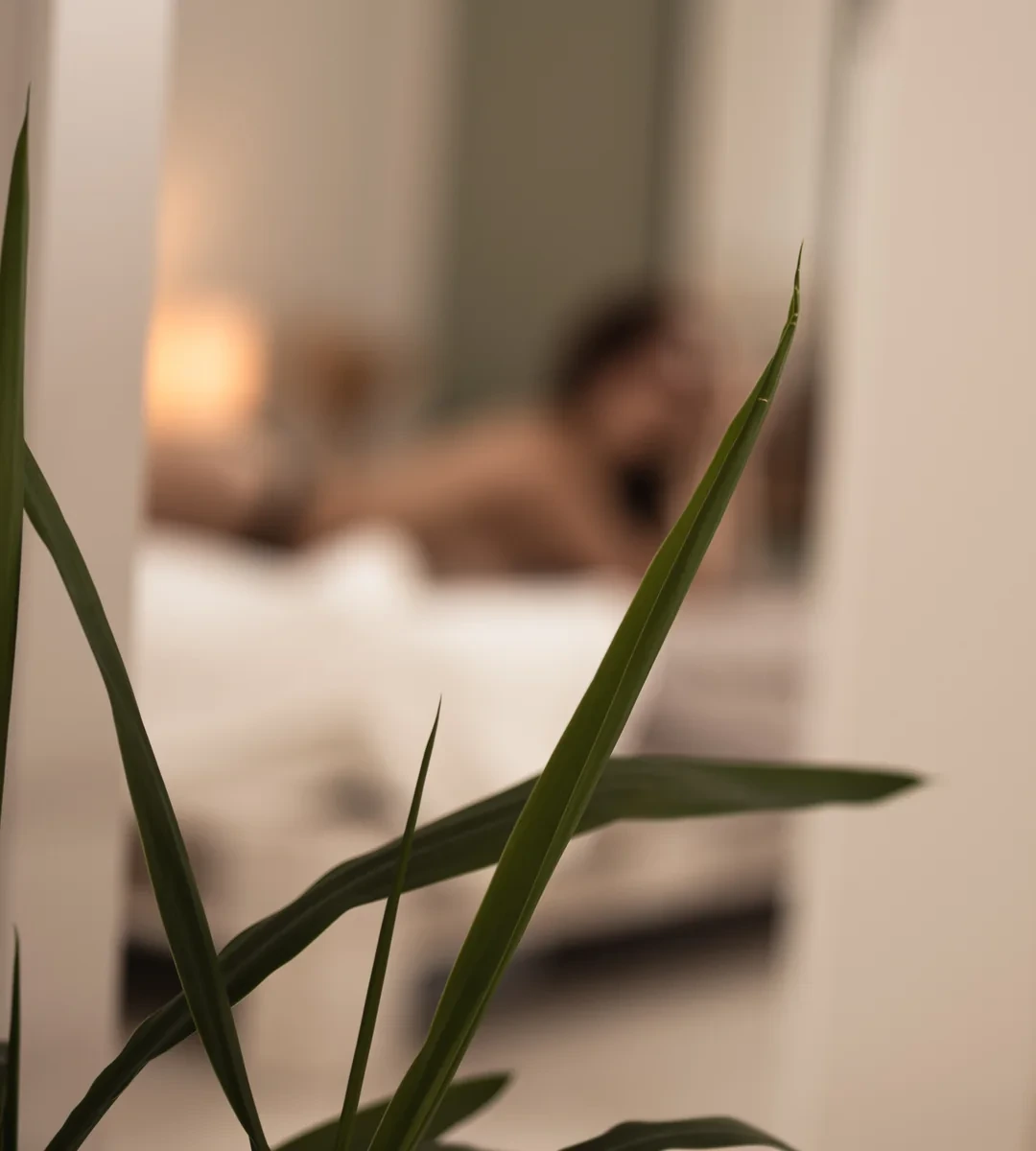 Ruhiger Boudoir-Moment auf einem Bett, durch die Blätter einer Pflanze gesehen.